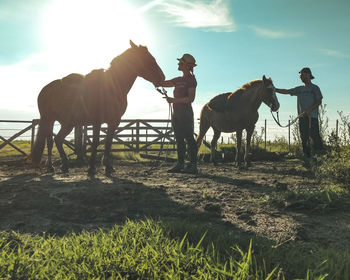 Two people riding horse on field against sky