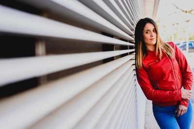 Portrait of beautiful woman standing by window blinds