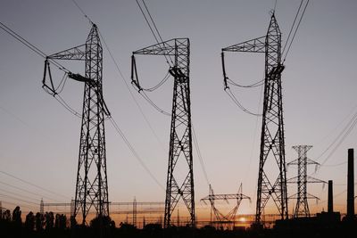 Low angle view of silhouette electricity pylons against sky during sunset