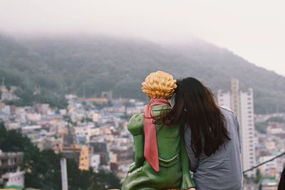 Rear view of woman sitting with sculpture against cityscape