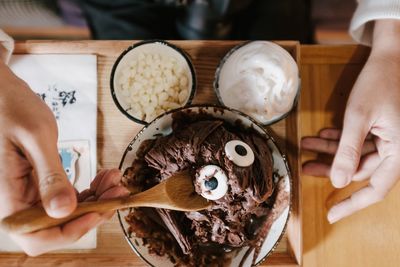 Cropped hand of person holding wooden spoon over chocolate dessert in bowl on table