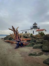 Lighthouse on beach by sea against sky