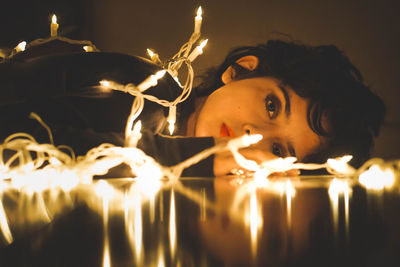 Portrait of woman with lying on floor by illuminated lights at home