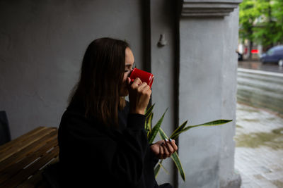 Young woman alone drinking a drink in a terrace cafe on a rainy day