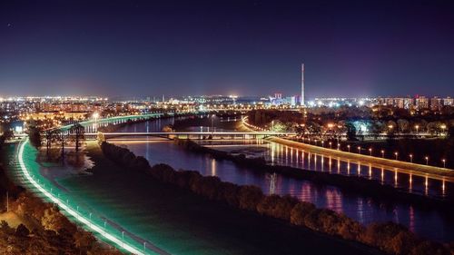 Illuminated bridge over river against buildings in city at night