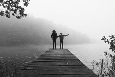Rear view of siblings on pier over lake during foggy weather