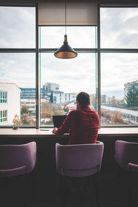 Rear view of man sitting on chair against window