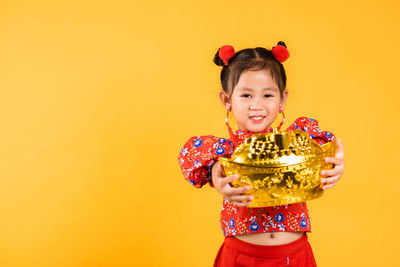 Portrait of smiling young woman standing against yellow background