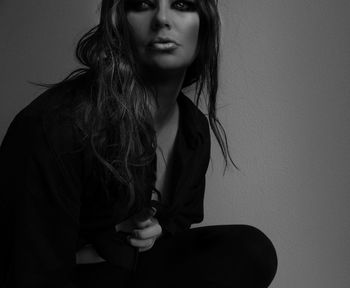 Young woman with long hair and make-up sitting against wall