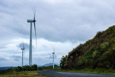 Low angle view of windmills on field against sky