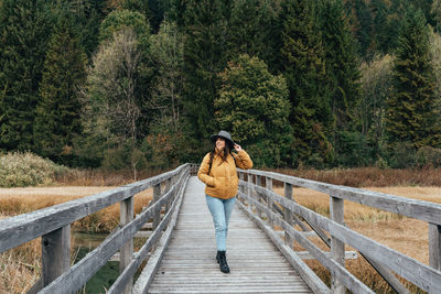 Young woman wearing autumn clothing, standing on wooden elevated path