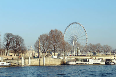 Ferris wheel by river against clear sky