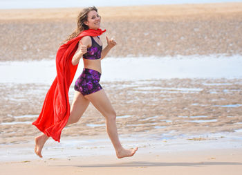 Full length of young woman wearing cape while running at beach