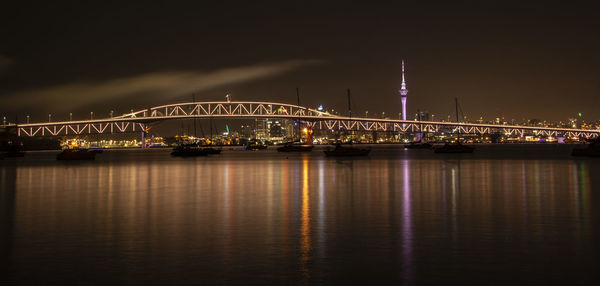 Illuminated bridge over river against sky at night