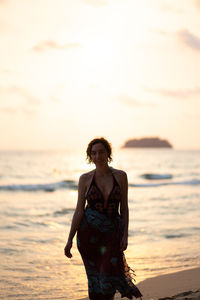 Woman standing at beach against sky during sunset