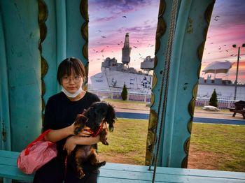 Portrait of teenage girl with dog standing against window