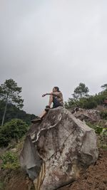 Young man on rock by land against sky