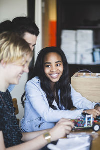 Smiling high school students preparing toy car at desk while teacher standing in classroom