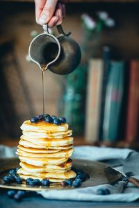 Cropped hand pouring honey on pancake