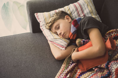High angle view of boy sleeping with hot water bottle on sofa at home