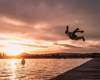 People jumping over lake against sky during sunset