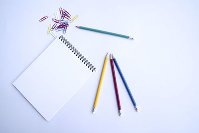 Directly above shot of colorful pencils and note pad on white background