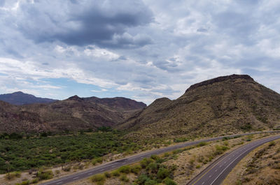 Country road leading towards mountains against sky