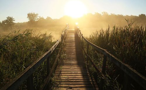 Walkway amidst field against sky during sunset