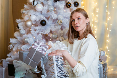 Smiling caucasian young woman opens box with christmas present. christmas