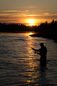 Silhouette man in lake against sky during sunset