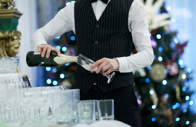 Midsection of waiter pouring champagne in restaurant