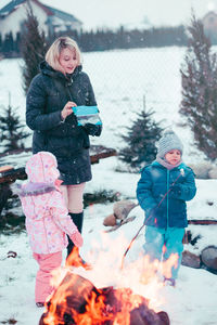 Mother with children standing on snow covered field at campfire