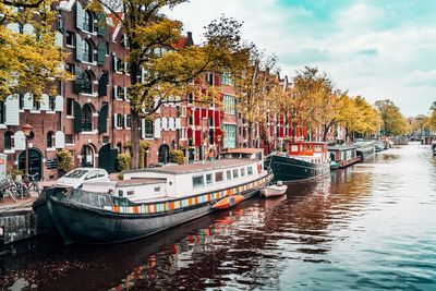 Boats moored in canal by city against sky