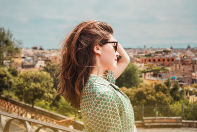 Profile portrait of young smiling woman in sunglasses with a panoramic view of rome, italy