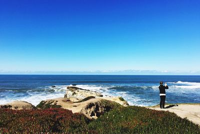 Rear view of woman standing by plants on cliff against sea