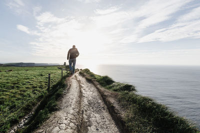 Rear view of man standing on mountain by sea against sky