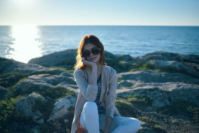 Young woman sitting on rock by sea against sky