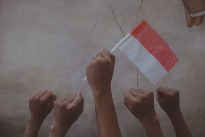 Cropped hands of people holding flag against wall