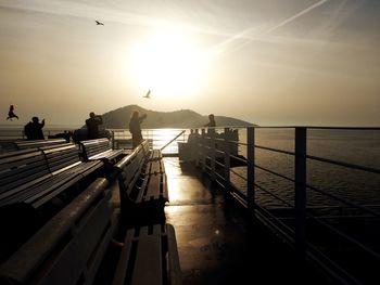 Silhouette people on pier over sea against sky during sunset