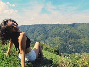 Side view of young woman sitting on landscape against sky