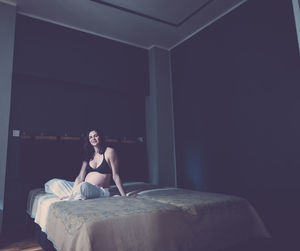 Portrait of smiling pregnant woman sitting on bed at home