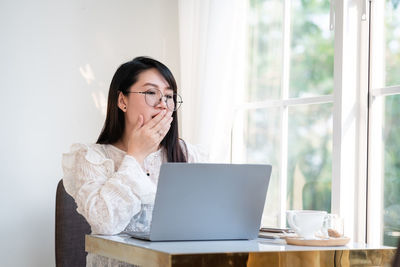 Young woman using phone while sitting on table