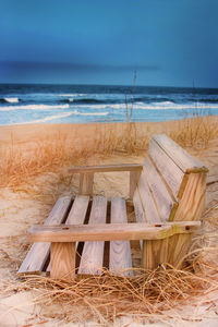 Wooden chairs on beach against sky