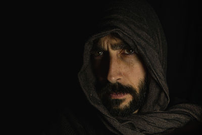 Face of a young man covering his face with a dark scarf on a black background