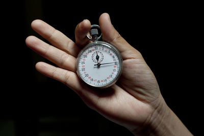 Cropped hand holding stopwatch against black background