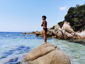 Young woman standing on rock by sea against sky