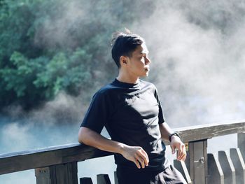 Young man looking away while standing on the lake