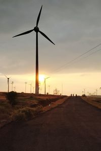 Wind turbines on field against sky during sunset