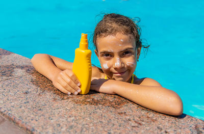Portrait of smiling girl with suntan lotion in swimming pool