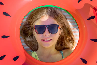 A girl in glasses smiles, holding an inflatable circle in her hands.
